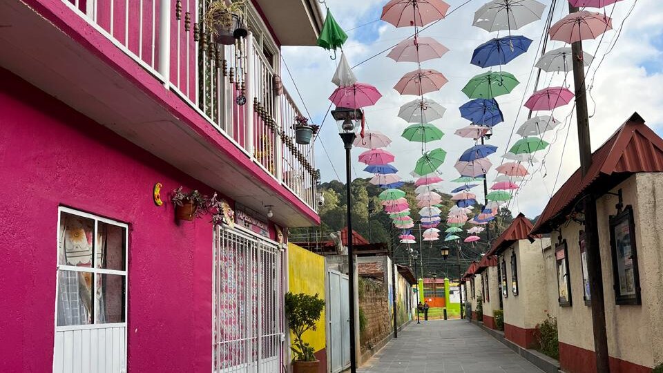 Callejón con fachadas coloridas y sombrillas colgantes suspendidas sobre la vía peatonal en Omitlán, Hidalgo.