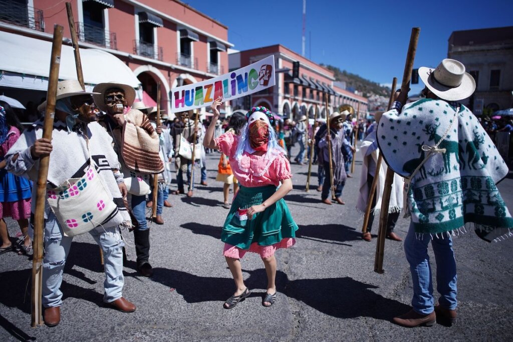Integrantes de una comparsa del municipio de Huazalingo participan en el Desfile “Es tiempo de Carnaval” 2026 en Pachuca, portando máscaras tradicionales, sarapes y un letrero con el nombre de su localidad.