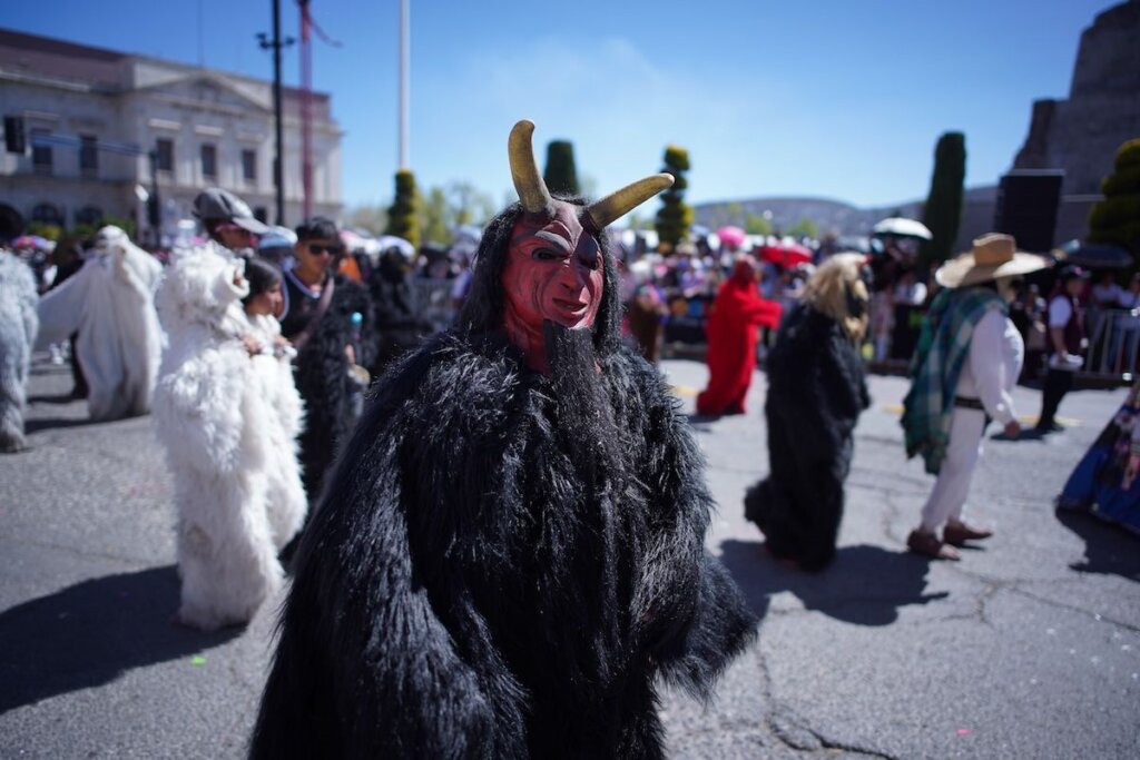 Integrante de una comparsa con máscara de diablo y traje tradicional recorre las calles del centro de Pachuca durante el Desfile “Es tiempo de Carnaval” 2026, acompañado de música de banda y cientos de asistentes.