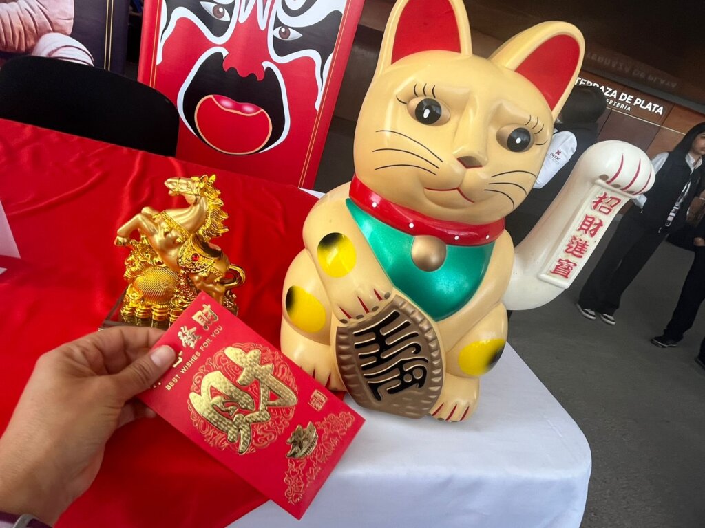 Figura del tradicional gato de la suerte (maneki-neko) junto a un caballo dorado y un sobre rojo con símbolos chinos, como parte del anuncio de la celebración Año Nuevo Chino 4724, Año del Caballo, en Pachuca.