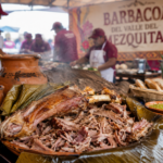 Plato tradicional de barbacoa hidalguense acompañado de salsa, pan y productos del maguey, en una ambientación inspirada en el Festival de la Barbacoa del Valle del Mezquital.