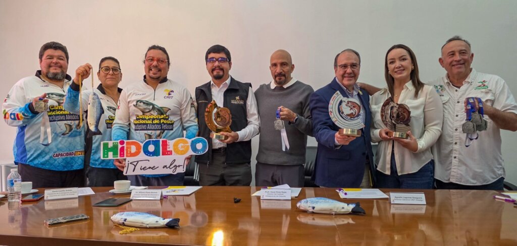 Autoridades estatales, organizadores y representantes del Campeonato Nacional de Pesca de Trucha Inclusiva posan con trofeos, medallas y artículos alusivos al evento durante la presentación oficial en Hidalgo.