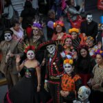 Grupo de participantes caracterizados como catrinas y catrines, con maquillaje de calaveras, trajes tradicionales y coronas de flores, durante un desfile de Día de Muertos en las calles de Pachuca, Hidalgo.