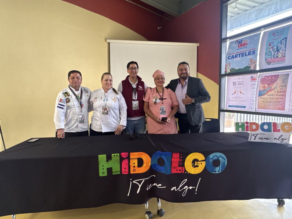 Cinco participantes de la presentación de “Tulancingo Entre Sabores” posan detrás de una mesa con el logotipo turístico de Hidalgo; dos visten filipinas de chef.